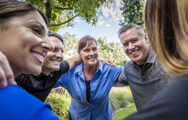 People standing in a circle with their arms linked on each others shoulders