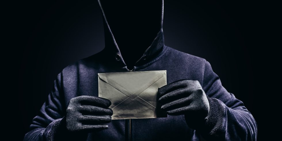 Photo of scary hooded man holding letter.